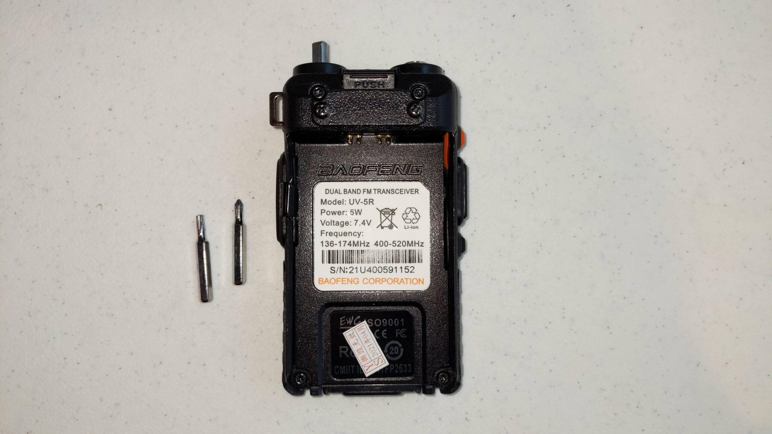 Rear of Baofeng UV5R, with battery removed and screwdriver bits for disassembly shown